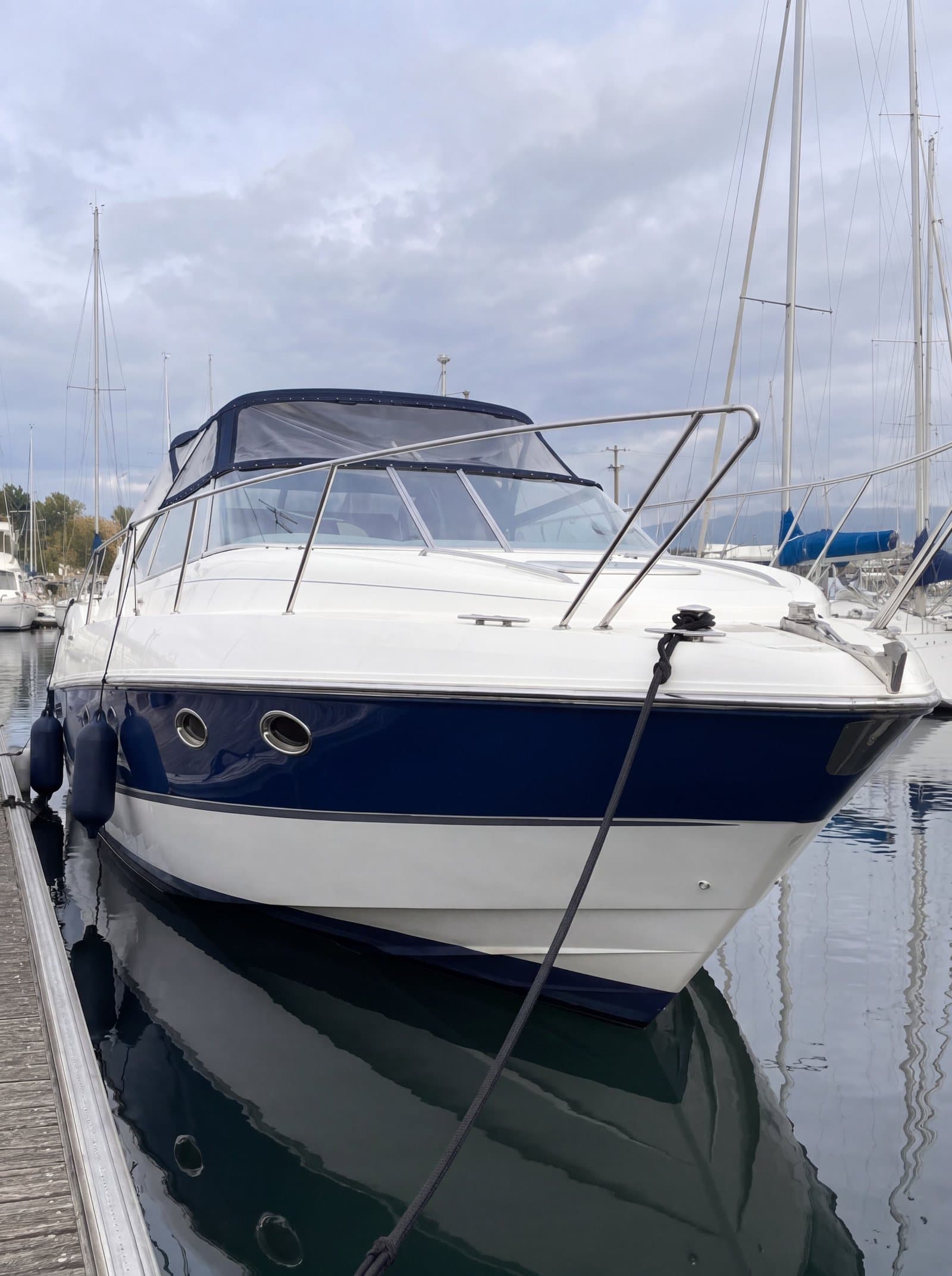 The same yacht after treatment, with a deep, glossy blue hull reflected in the water